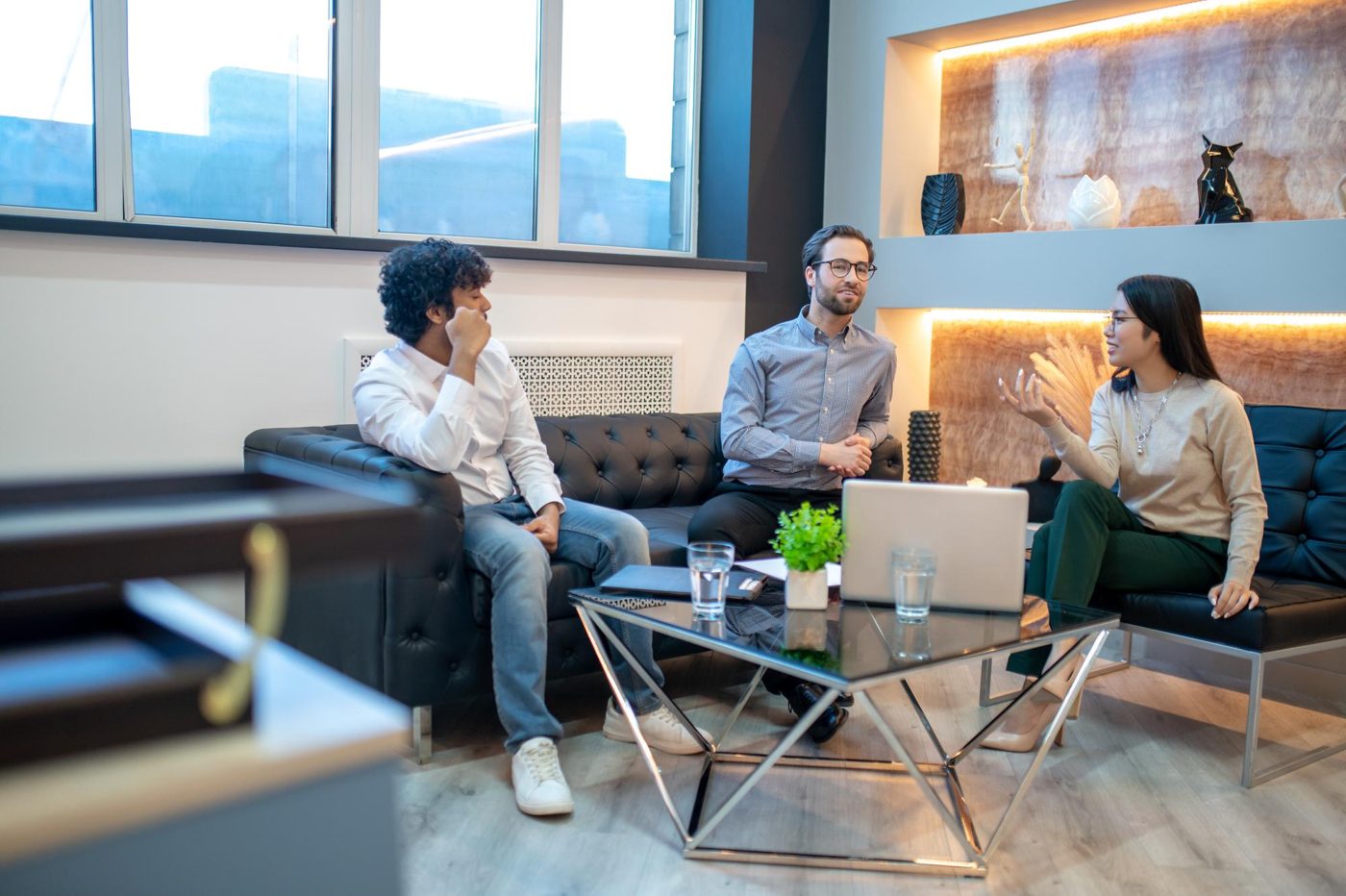 Three colleagues in a discussion around a table with a laptop