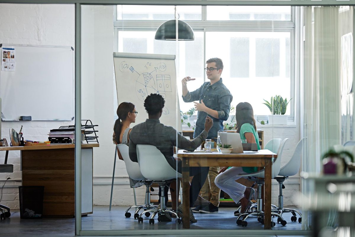 A team watching a colleague present findings at a whiteboard